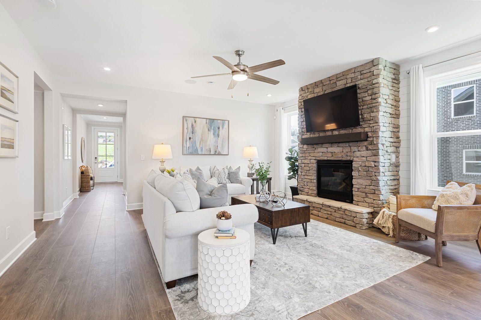 great room area with hardwood floors, two white couches, and a stone-faced fireplace