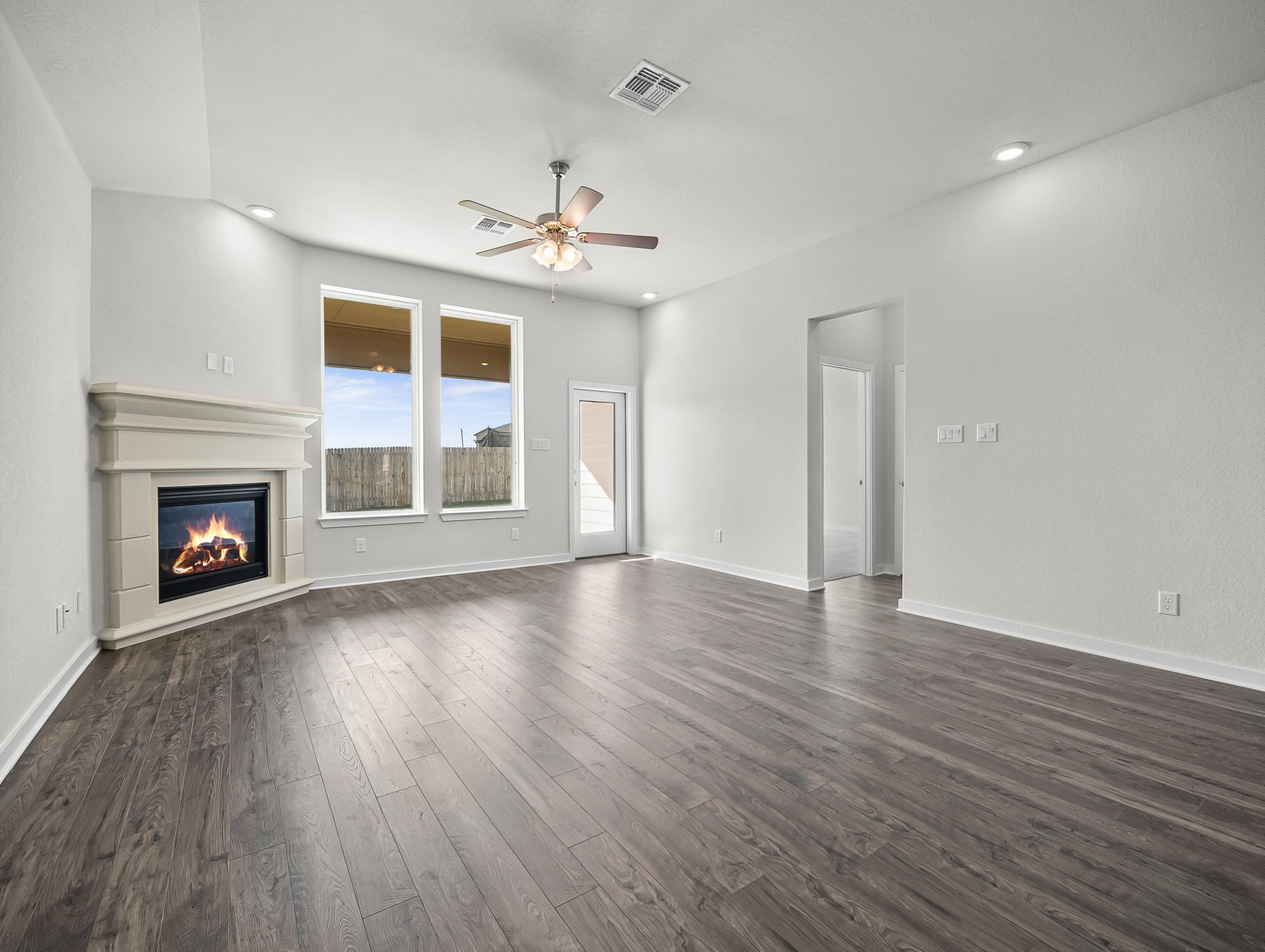 great room with brown flooring, windows & a ceiling fan