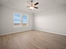 bedroom with brown flooring, windows & a ceiling fan